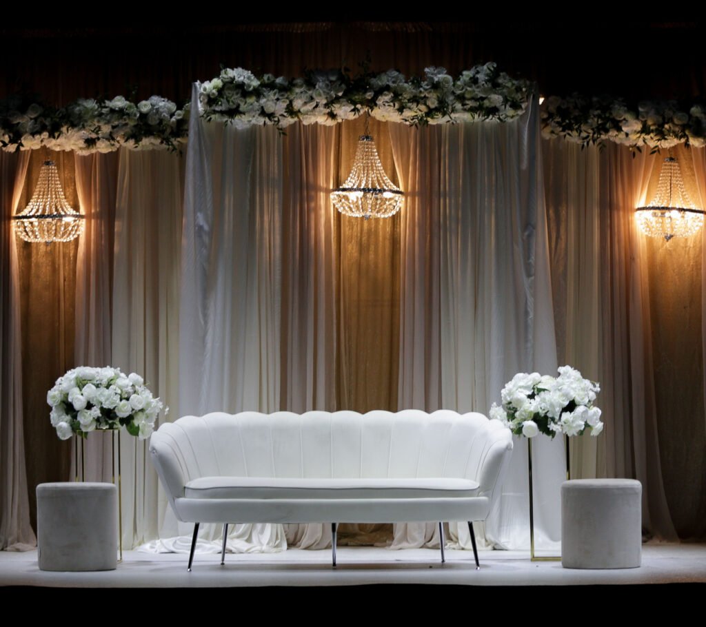 Dekorert bryllupsscene med hvit sofa, blomster og lysekroner i bryllupslokale i Vestby